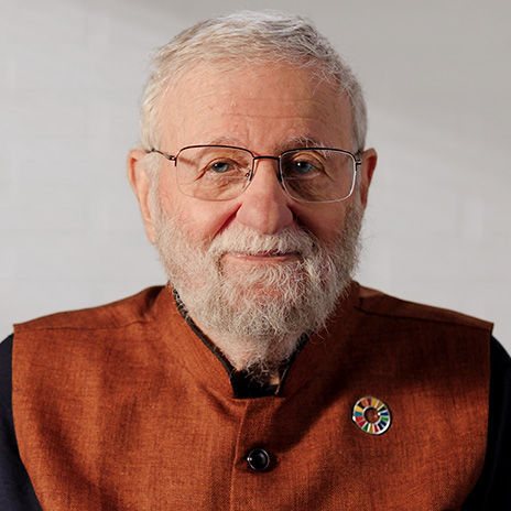 عکس پرترهٔ دان نورمن، مردی مسن با موی سفید، ریش سفید کوتاه و عینک، با پیراهن قهوه‌ای